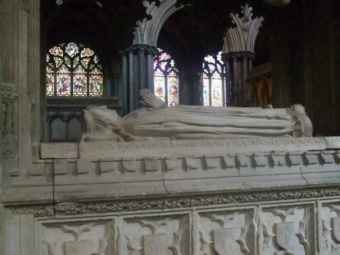 Stone effigy of a noble from the Middle Ages, with stained glass windows in the background.