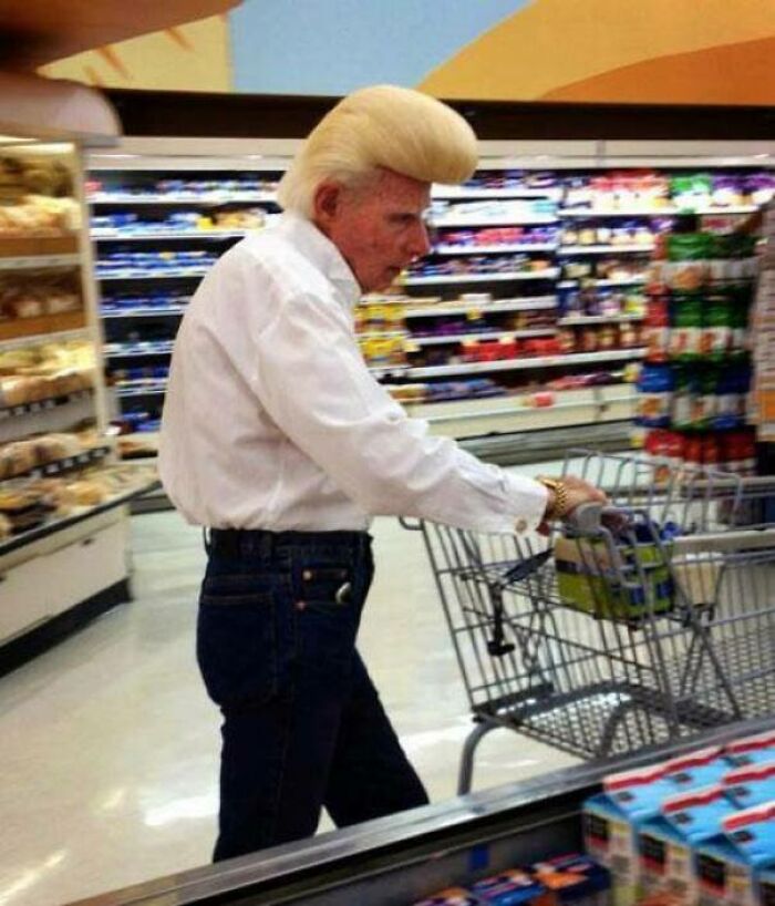 An older man with a dramatically bold, high blonde pompadour hairstyle pushing a shopping cart in a grocery store.