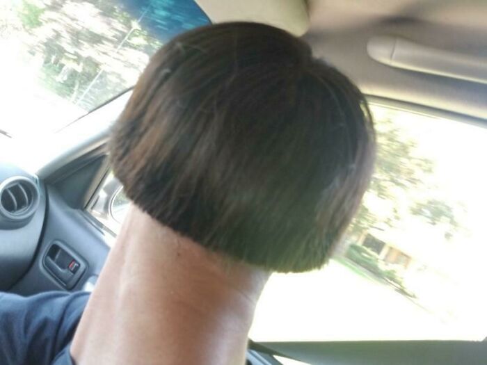 A person in a car with a very short, bowl-cut hairstyle, barely covering the top of their head and showing a long neck.