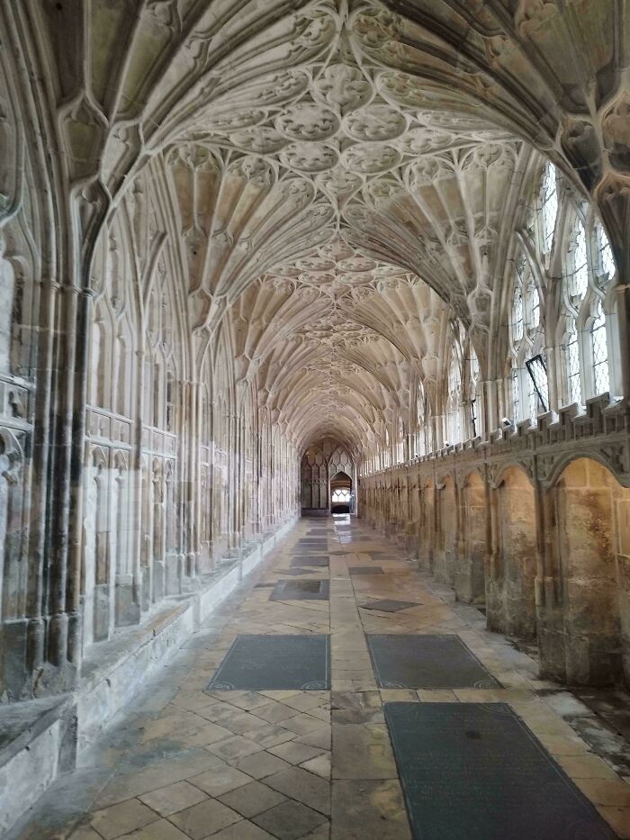 A long, arched hallway with intricate stone carvings on the ceiling and walls, typical of the Middle Ages.