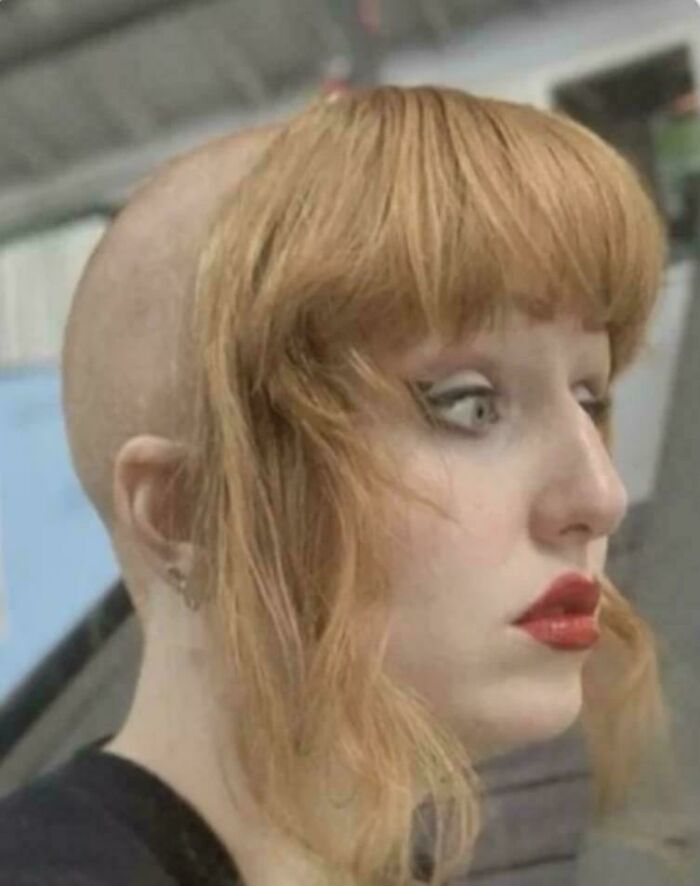 A person with a shaved head and a section of blonde, bold hairstyles framing their face.