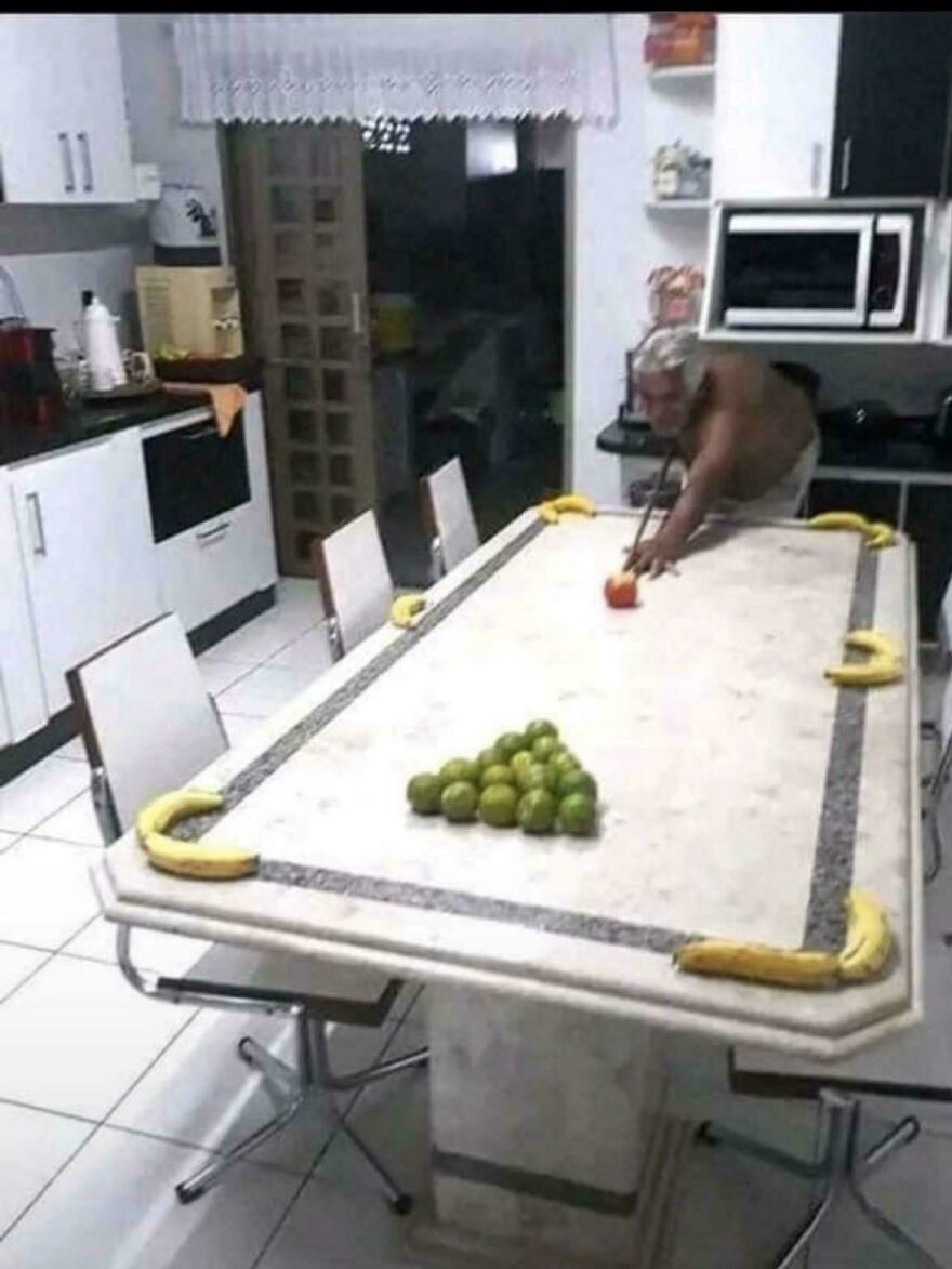 An old man playing pool on a marble table with limes as balls and bananas as cushions, a hilarious meme inspired by real life.