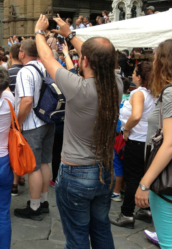A man with long dreadlocks and a receding hairline, standing in a crowd, displaying bold hairstyles.