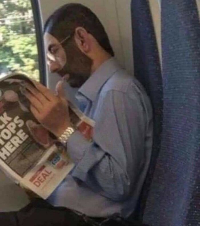 A person on a train reading a magazine, sporting a distinctive beard and bold hairstyles.