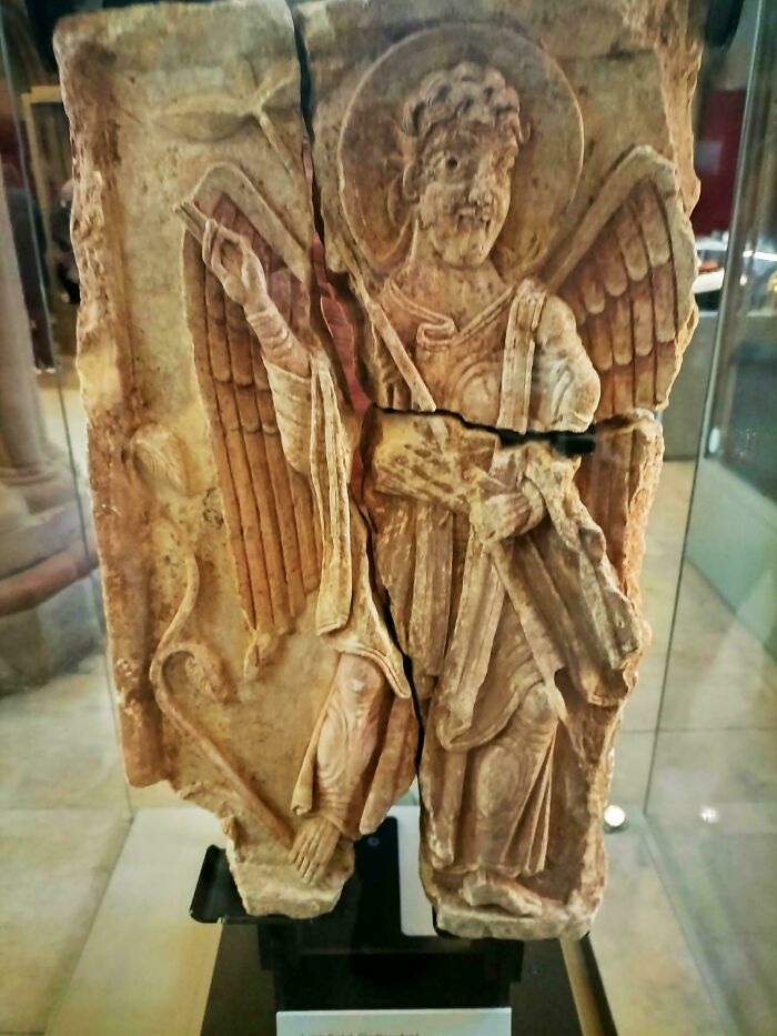 A broken stone carving of an angel with wings and a halo, a significant historical artifact from the Middle Ages.