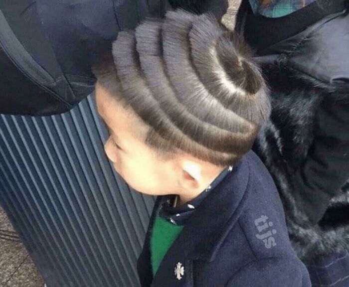 A young boy with a bold, sculptured hairstyle, featuring swirling patterns shaved into his hair.