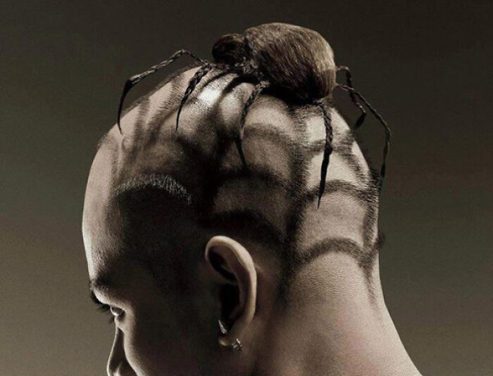 A person with a bold hairstyle featuring a spider-web design shaved into the back of the head and a spider bun.