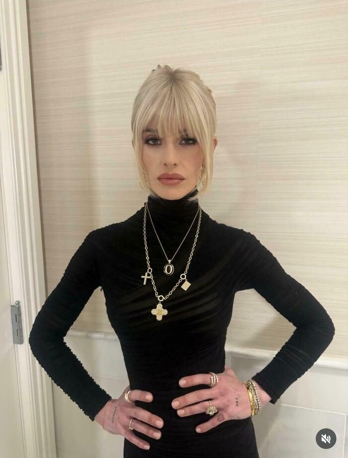 A woman in a black turtleneck and multiple necklaces strikes an unnatural pose for social media.