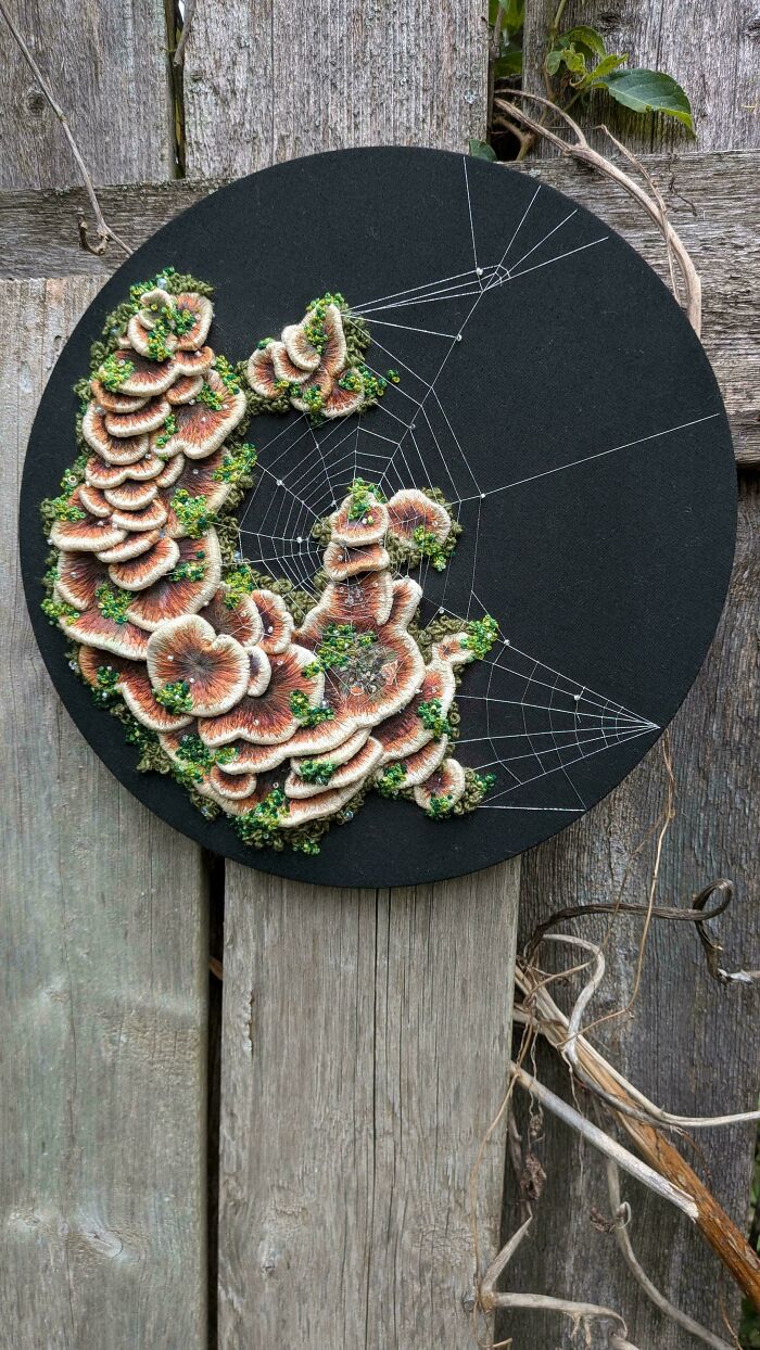Detailed embroidery projects depicting textured mushrooms and a delicate spiderweb on black fabric