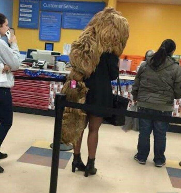 A woman in a black dress with an incredibly long, shaggy blonde hairstyle trailing to the floor, waiting in line.