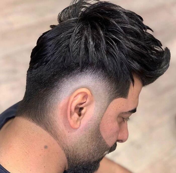A man's bold hairstyle featuring a sharp fade and a sculpted beard line, showcasing a modern haircut.