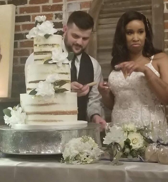 Funny wedding photo of a bride reacting to a groom cutting their iconic wedding cake.