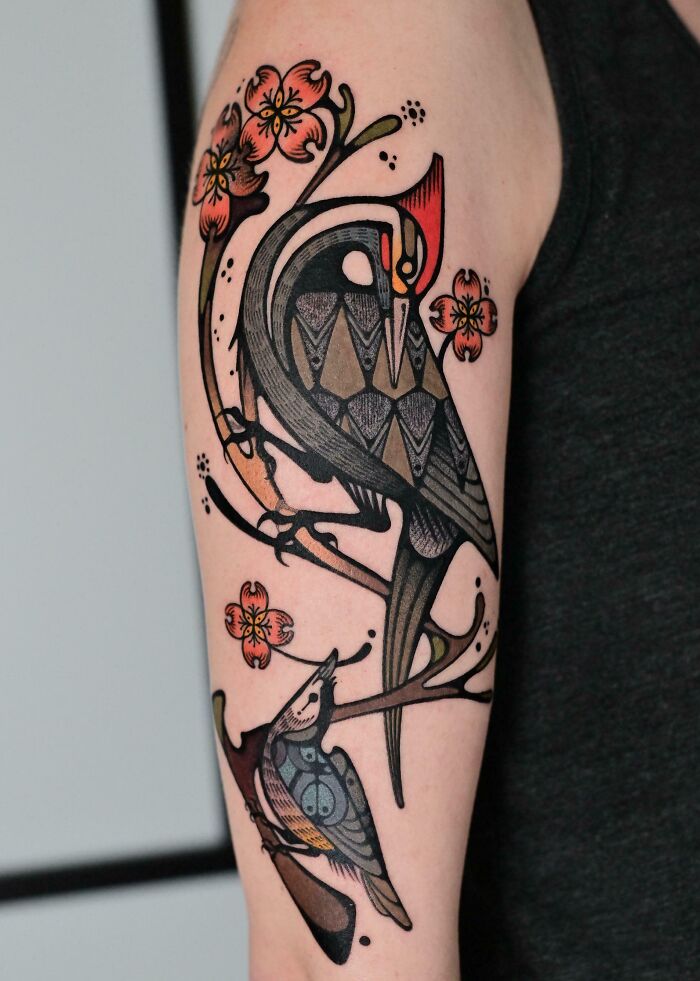 A colorful arm tattoo of two stylized birds perched on branches with flowers, featuring stunning tattoos.