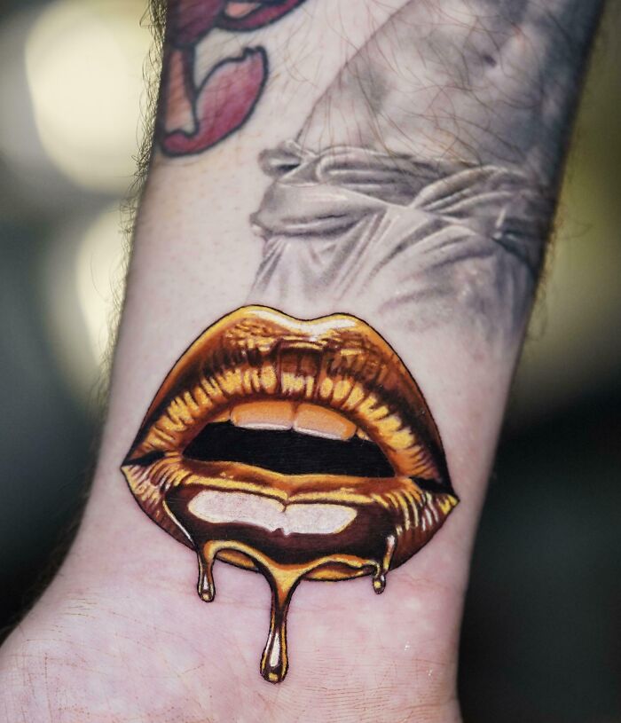 A vibrant tattoo of golden lips with dripping honey on a person's wrist, highlighting stunning tattoos.