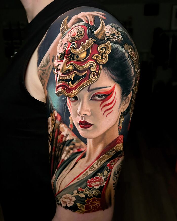 A detailed tattoo on a shoulder depicting a woman in traditional Japanese attire with a red and gold Hannya mask. A stunning tattoo.