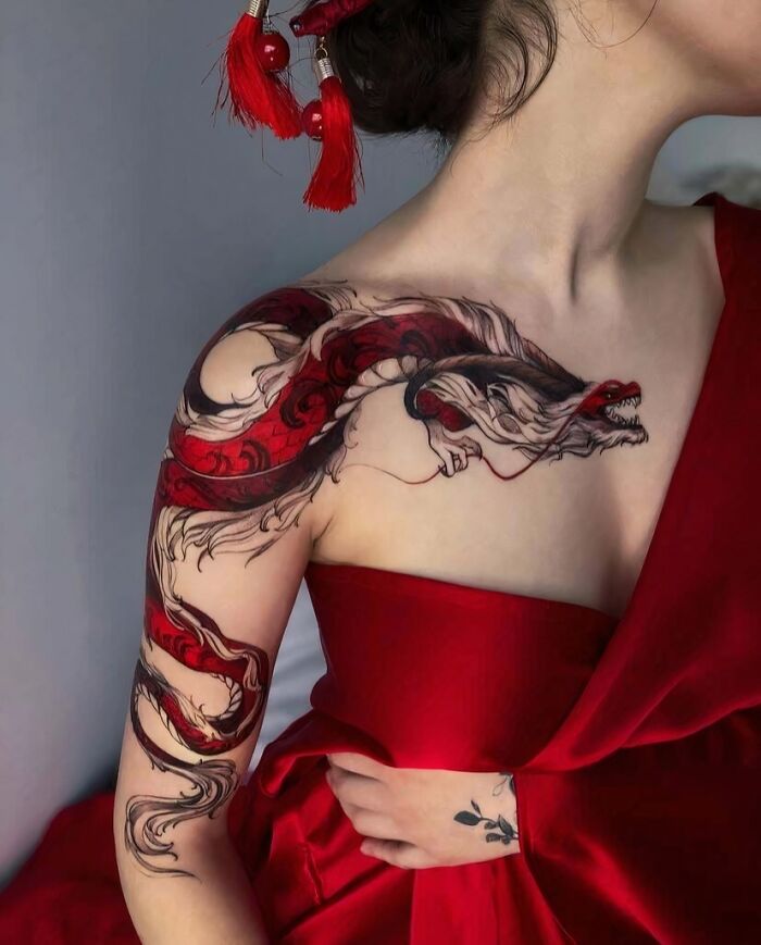 A stunning tattoo of a vibrant red and white dragon design covering a woman's shoulder and chest.