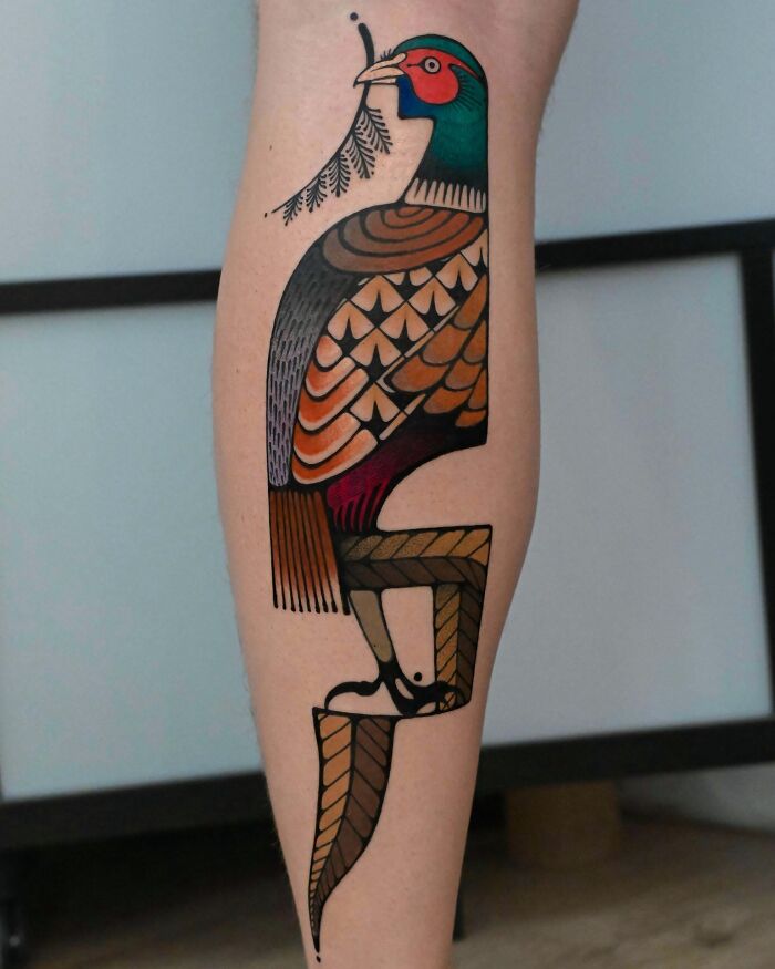 A stunning tattoo of a stylized pheasant with intricate feather details on a person's leg.
