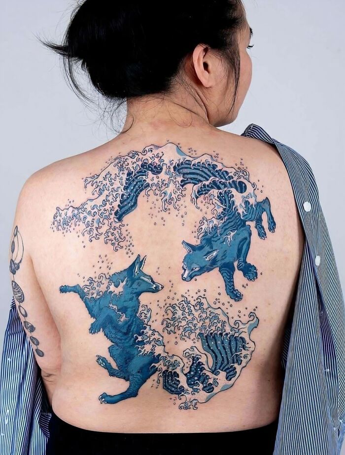 Woman's back adorned with stunning tattoos featuring blue wave patterns forming animal shapes, a unique body art.