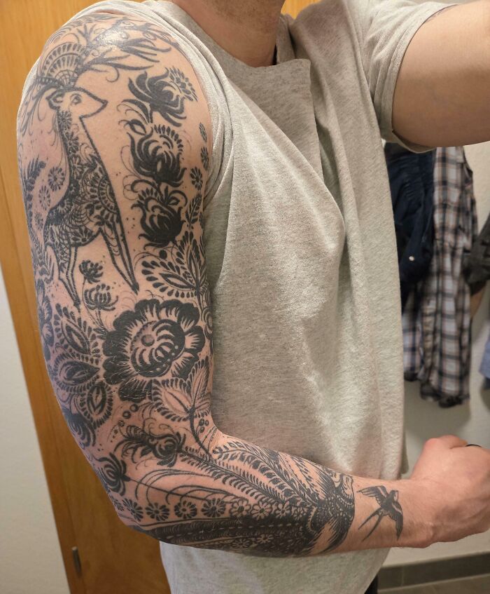 A man's arm with a stunning black and grey floral and animal sleeve tattoo, showing off a happy choice.