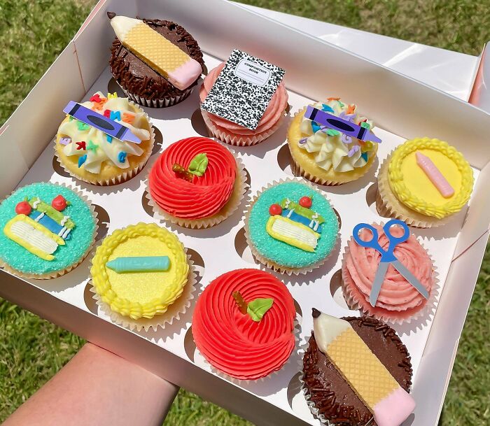 A box of school-themed cupcakes, with pencils, notebooks, and crayons. Bakers prove treats look amazing and taste delicious.
