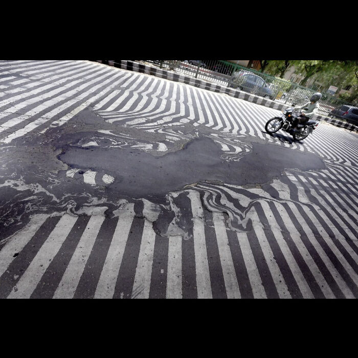 A street crosswalk with painted white stripes is warped and melting due to scorching summer temperatures, showing summer ruining everything.
