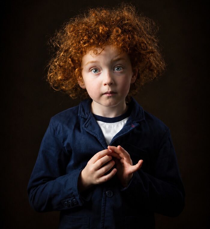 A captivating portrait of a young boy with bright blue eyes and a shock of curly natural red hair.