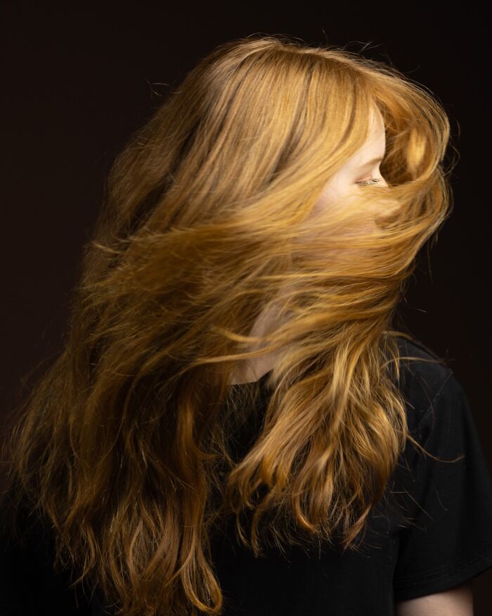 A beautiful natural redhead woman with long flowing hair covering her face, from a global portrait project.