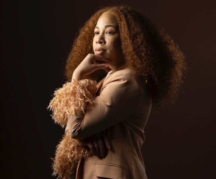 Portrait of a natural redhead woman with voluminous curly hair and a thoughtful expression.