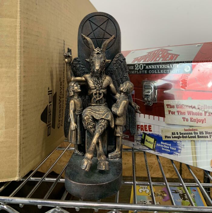 A Baphomet statue with children, a jackpot discovery from a thrift store, sitting on a shelf surrounded by boxes.