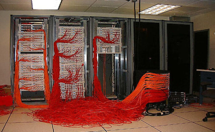 A room full of server racks with an incredibly messy tangle of red and orange ethernet cables, creating a confusing pic.