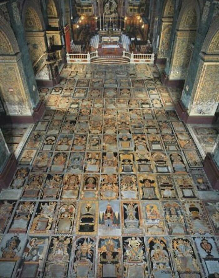 An ancient church interior with numerous intricately decorated tomb slabs on the floor, a confusing pic.