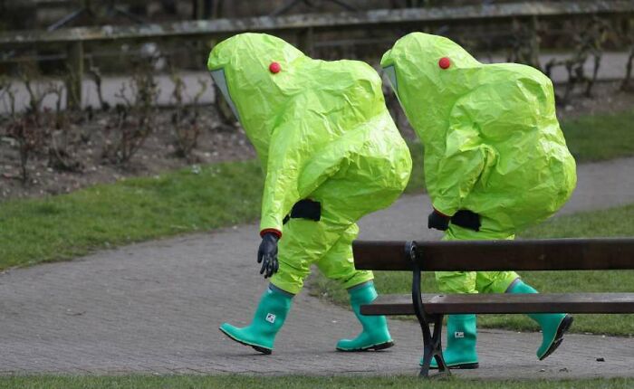Confusing pic of two people in hazmat suits walking in a park, with misleading headlines.