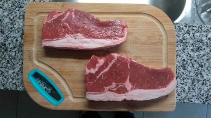 Confusing pics of two raw steaks resembling shoes on a wooden cutting board.