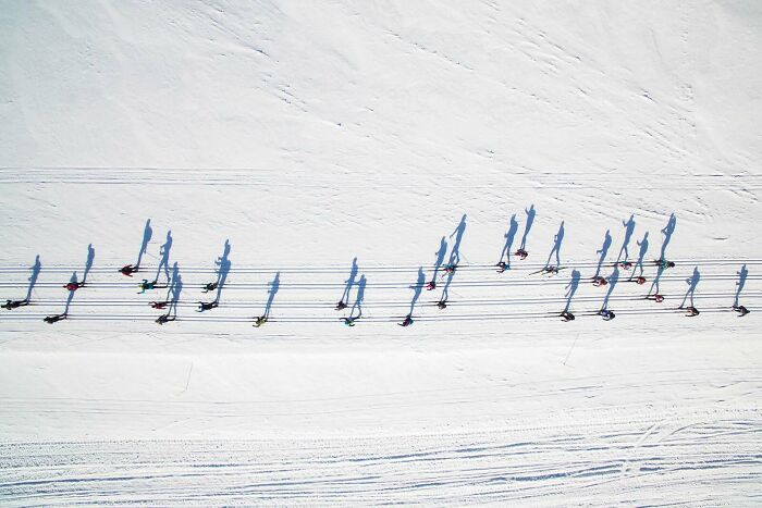 An aerial view of people skiing on snow with long shadows, a confusing pic.