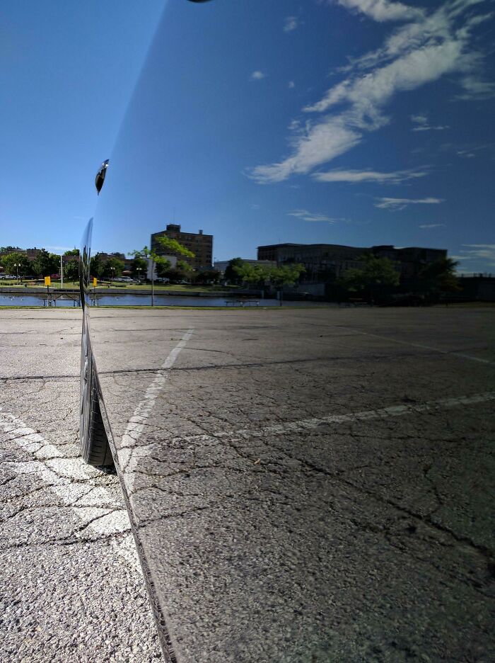 A highly reflective black car parked on asphalt, creating a confusing pic with a misleading reflection of the sky.