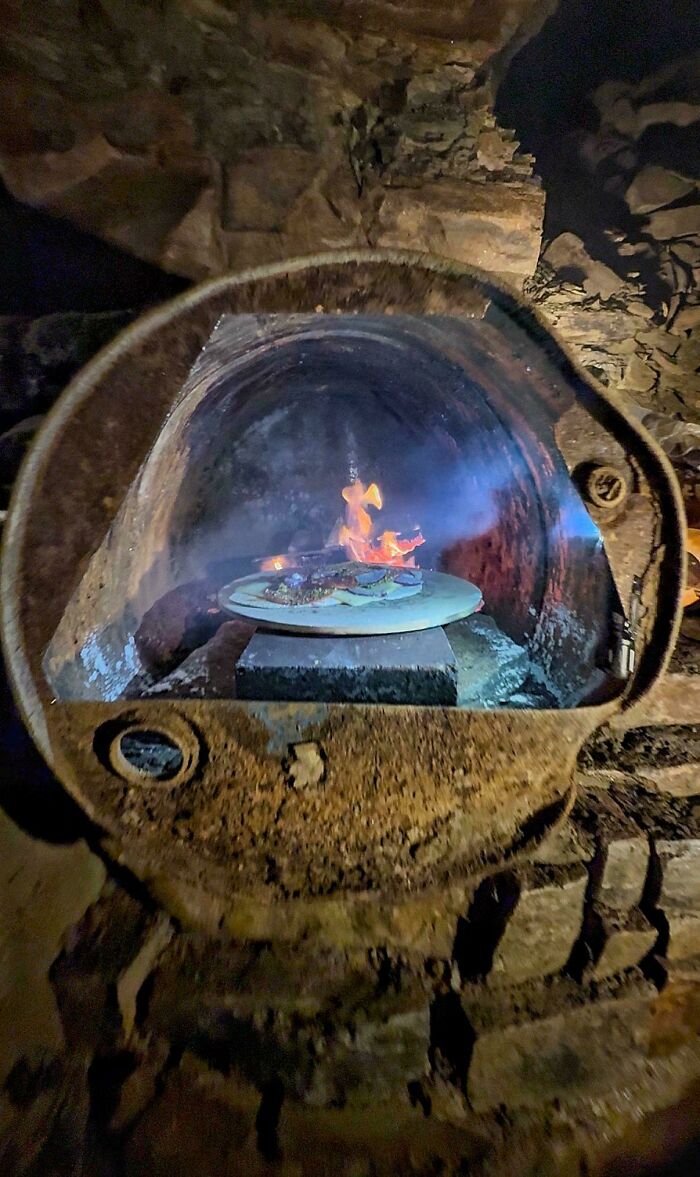 A pizza cooks inside a makeshift wood-fired oven, highlighting dangerous things people did.