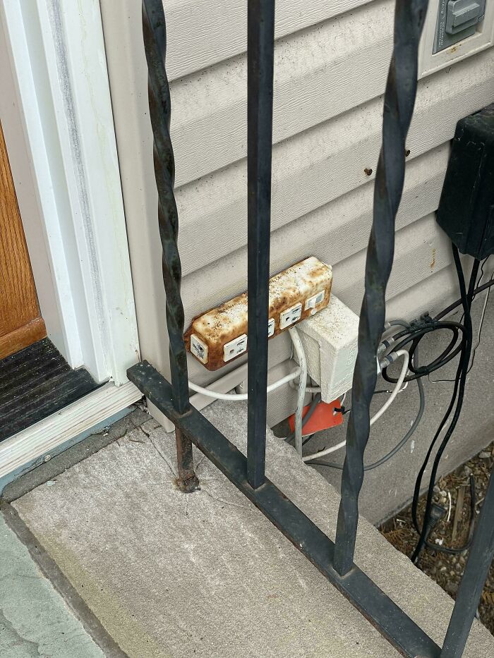 A dangerous and rusted outdoor power strip and exposed wiring on a concrete step, an unnecessary risk.