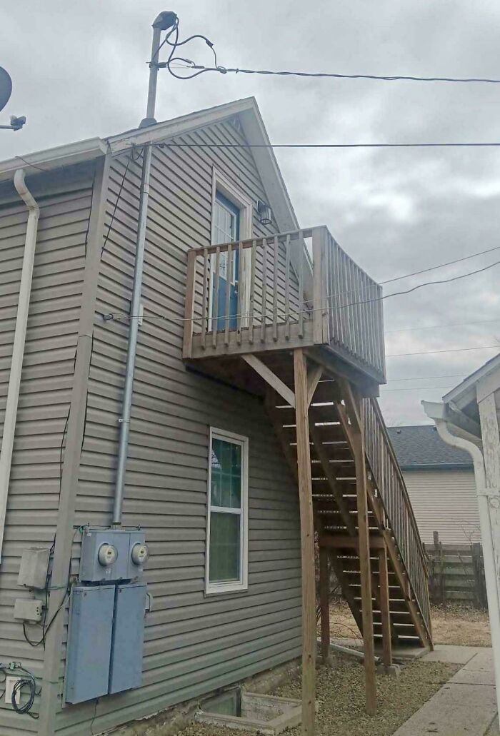 A dangerously constructed external wooden staircase leading to a second-story door on a house.