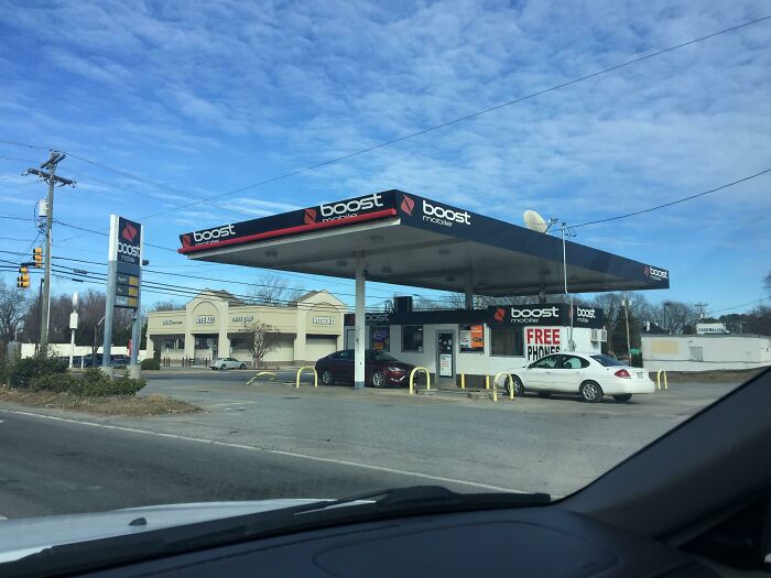 A former gas station building pretending to be a Boost Mobile store under a bright sky with cars at the pumps.