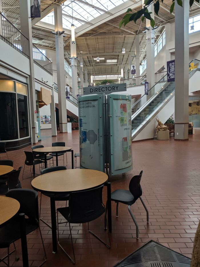 An empty shopping mall interior with tables, chairs, and a directory, one of many buildings pretending to be something else.