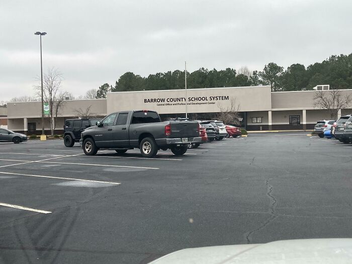 A building pretending to be something else, labeled Barrow County School System, with cars in the parking lot.