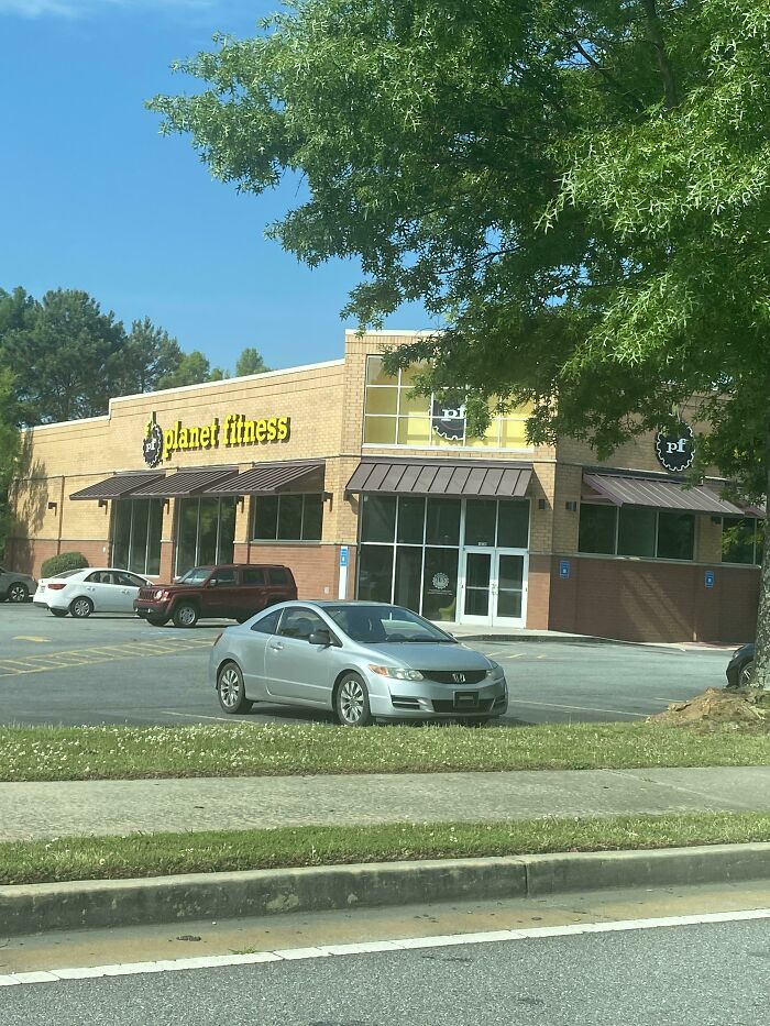 A Planet Fitness gym in a building pretending to be something else, with a brick exterior and a brown awning.