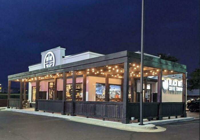 A Black Rock Coffee Bar with outdoor seating and string lights, a building pretending to be something it's not.