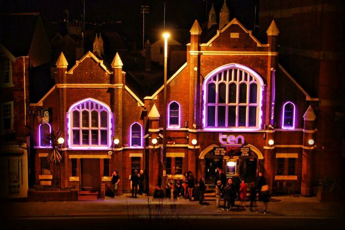 An old brick church building at night, now illuminated with purple lights, pretending to be a modern venue.