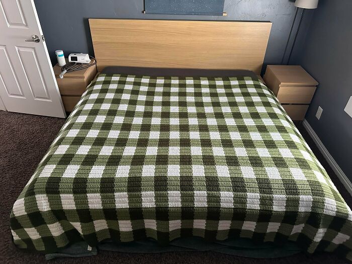 Green and white crochet blanket with checkered design on bed