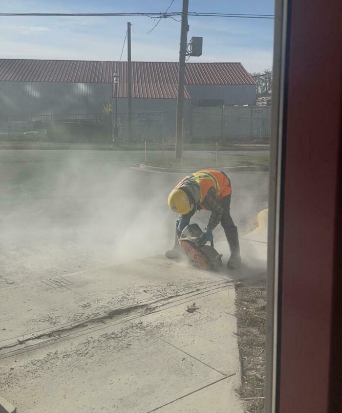 A worker operating a concrete saw, creating dangerous dust without proper protection, an unnecessary risk.