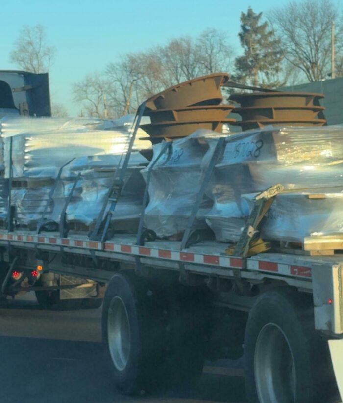 A flatbed truck with an unsecured load, including large metal pieces, creating dangerous conditions on the road.