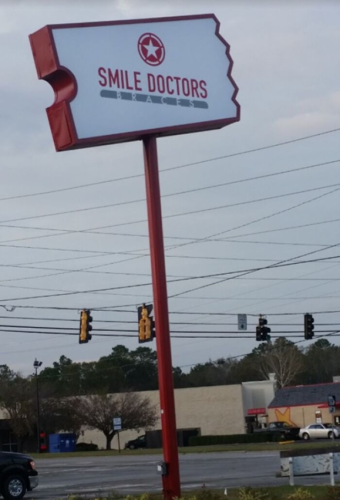 A sign for Smile Doctors Braces on a red pole, a building that is pretending to be something it is not.