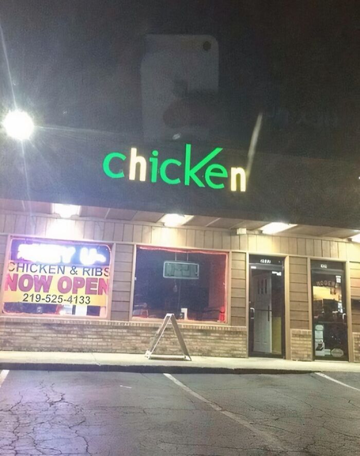 A building pretending to be something it is not; a neon green chicken sign above a storefront at night.
