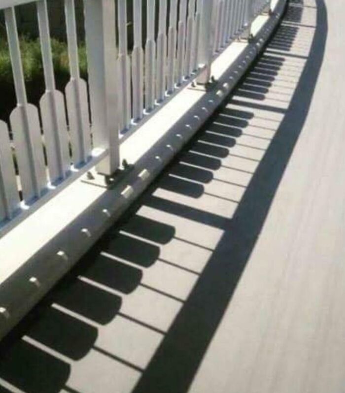 Confusing pic where the shadows from a white railing on a bridge look like piano keys.